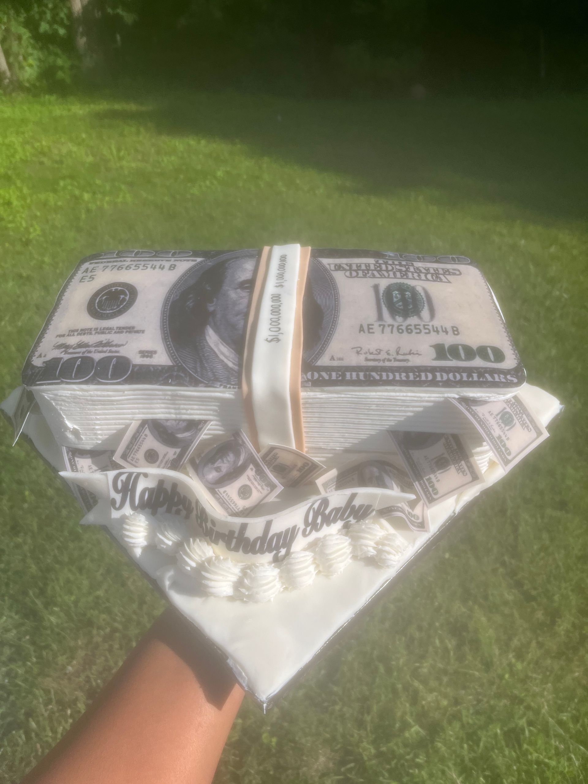 A person is holding a cake that looks like a stack of money.