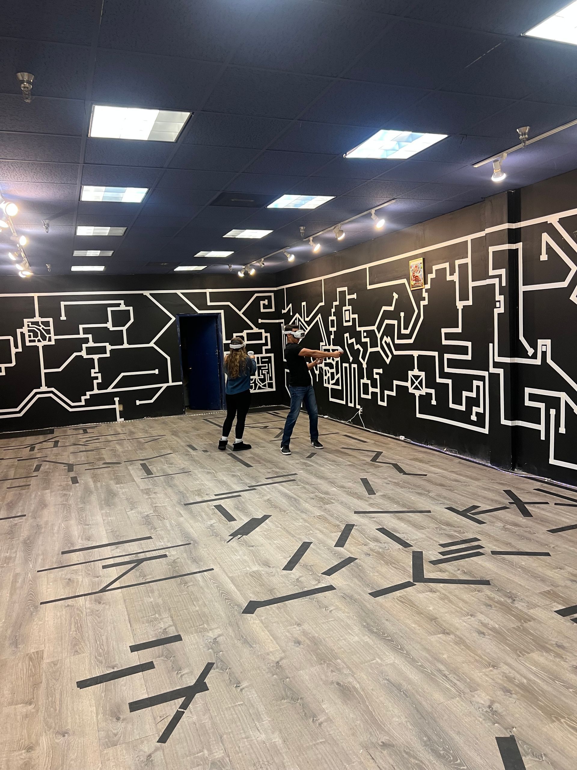 Two people stand in a room with black walls and white line art. Floor has matching patterns.