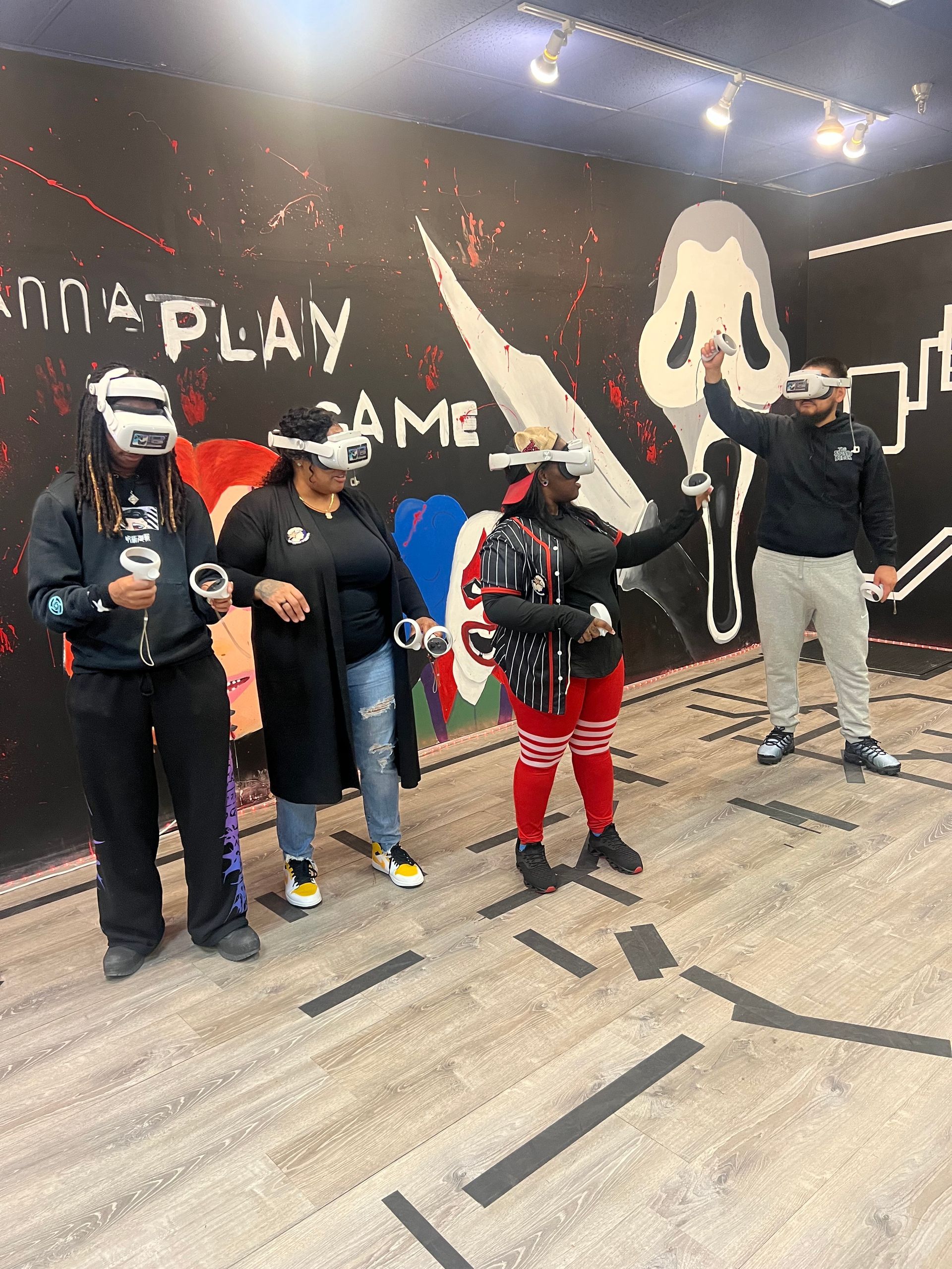 Four people wearing VR headsets play a game in a room with graffiti art. One person raises their arms.