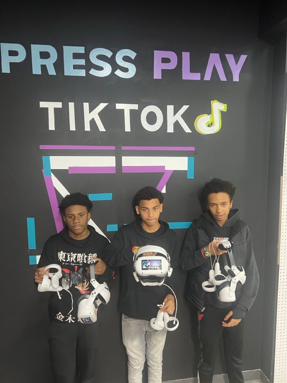 Three boys are standing in front of a wall that says press play tiktok
