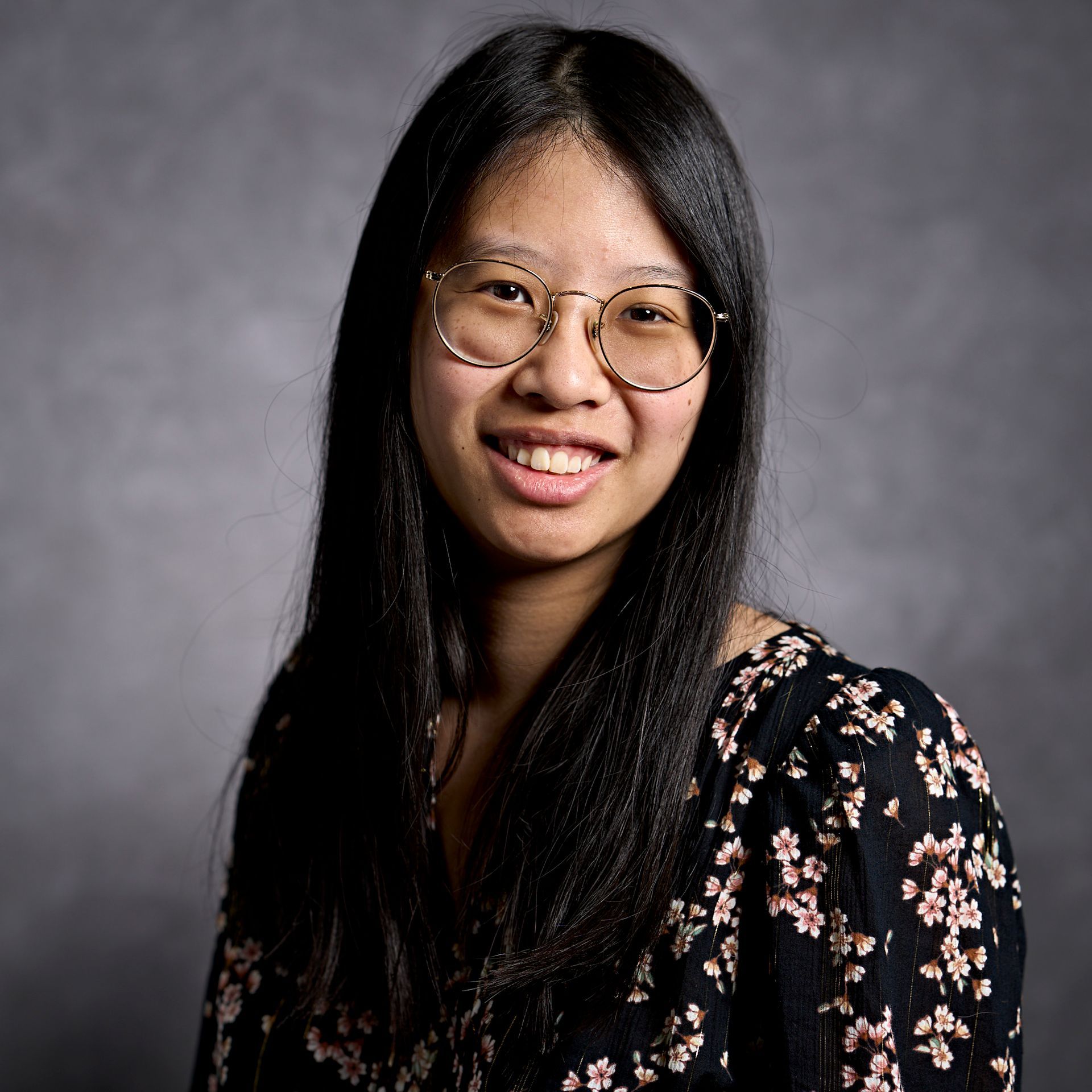 A woman wearing glasses and a floral shirt is smiling for the camera.