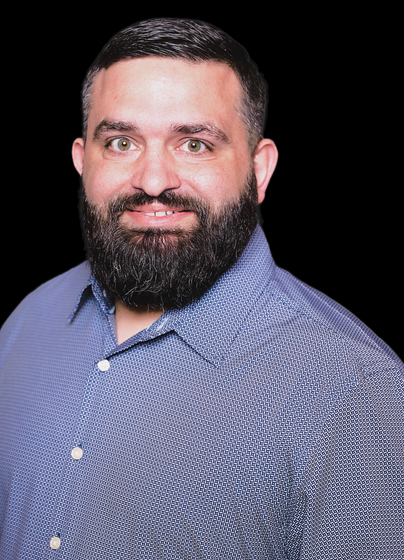 A man with a beard is wearing a blue shirt and smiling.