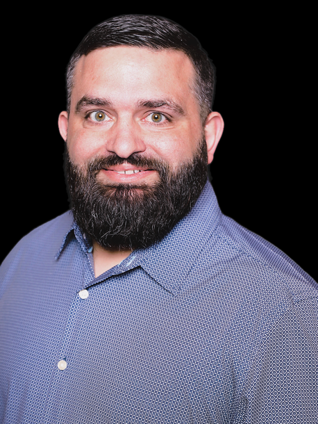 A man with a beard is wearing a blue shirt and smiling.