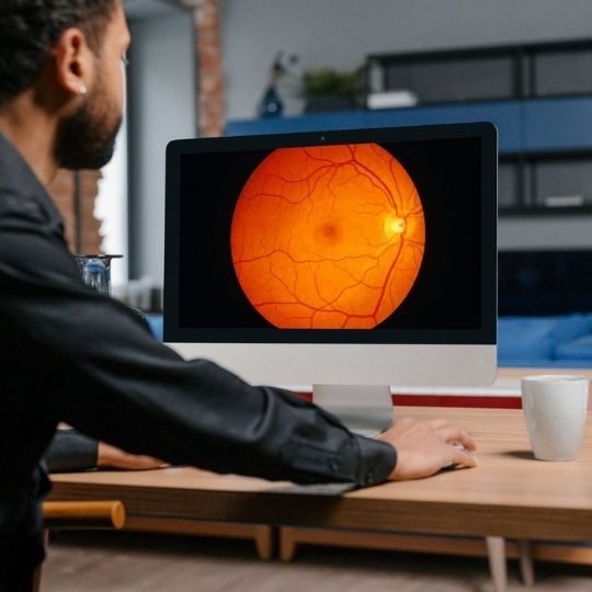 A man is sitting at a desk looking at a computer screen with an image of an eye on it
