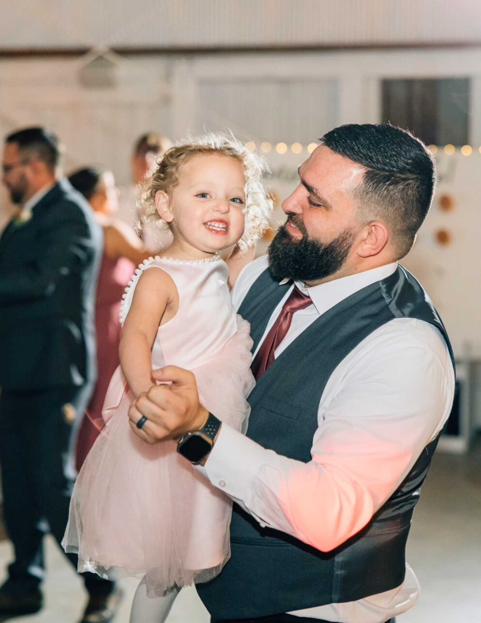 A man is holding a little girl in his arms while dancing at a wedding reception.