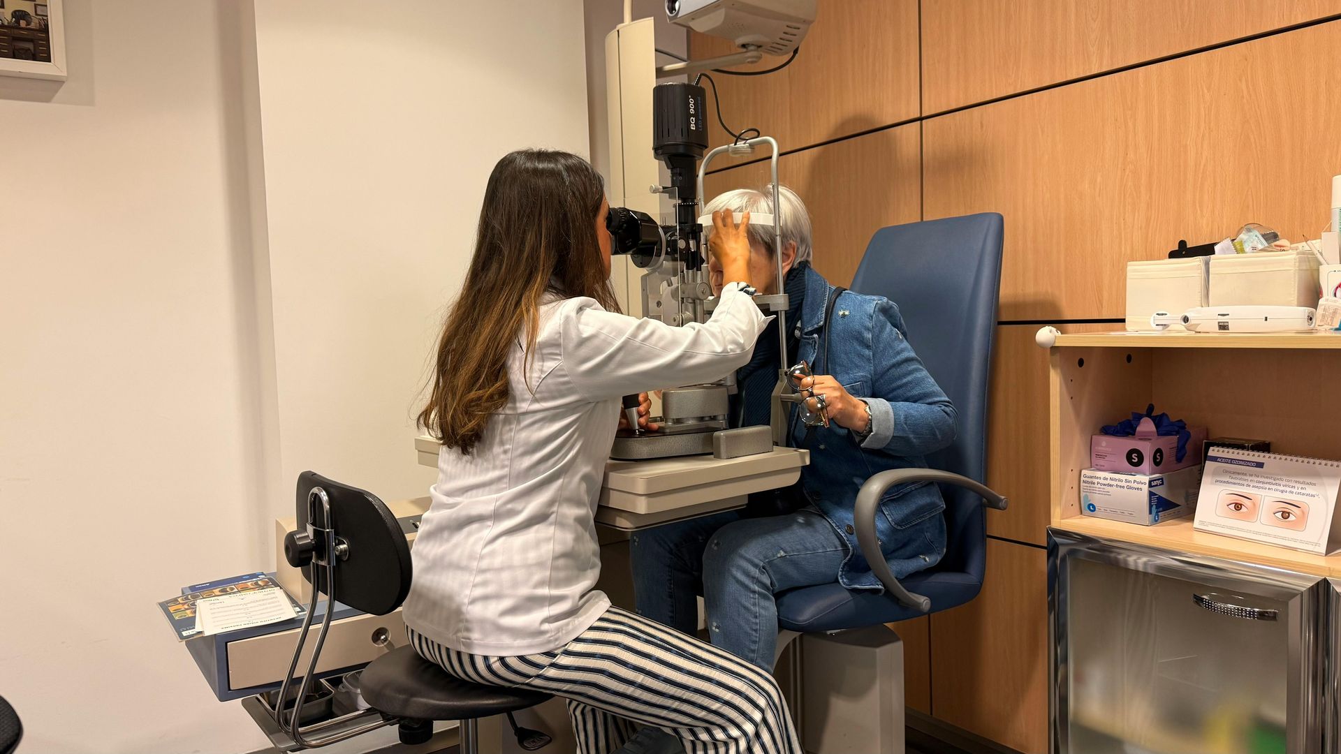 A woman is sitting in a chair getting her eyes examined by an ophthalmologist.