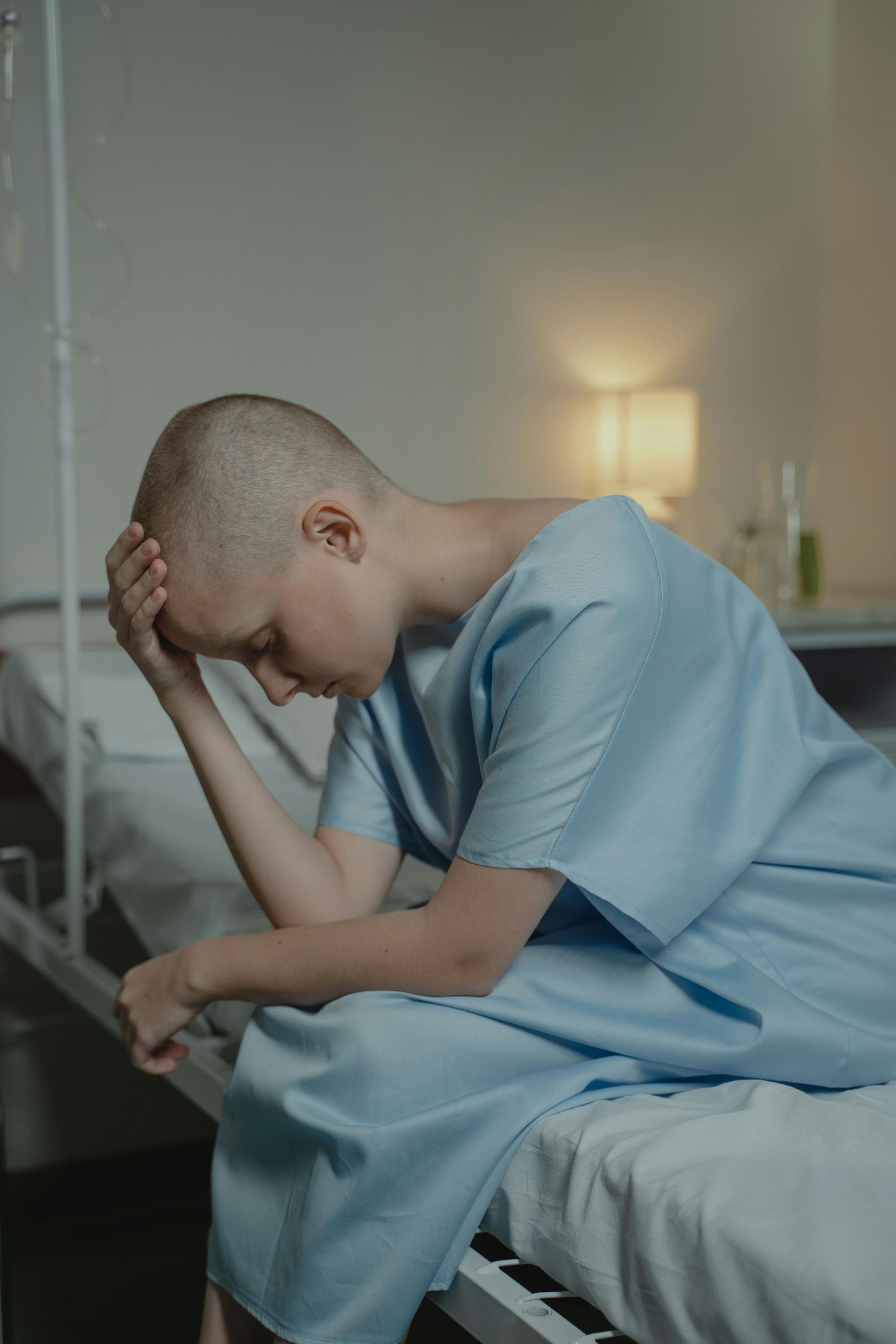 A woman with cancer is sitting on a hospital bed with her head in her hands.
