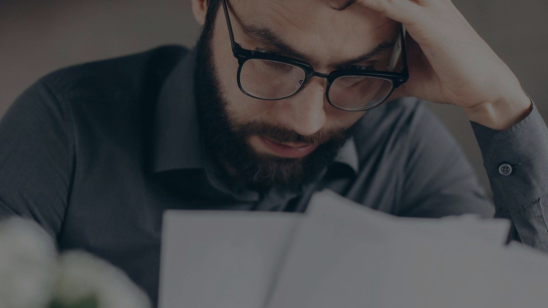 A man with a beard and glasses is looking at a piece of paper.