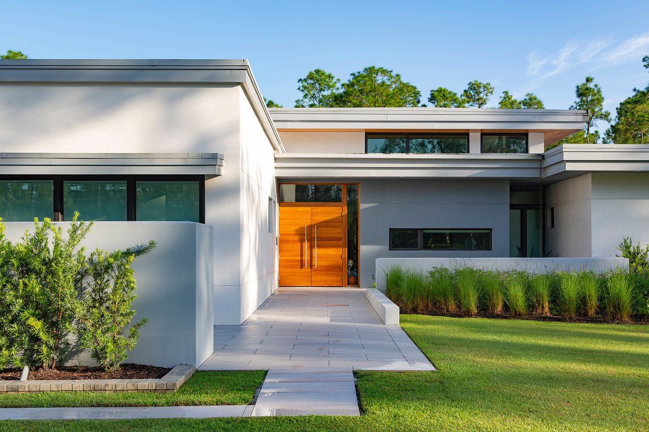 a tropical modern home with a wooden door and a walkway leading to it.
