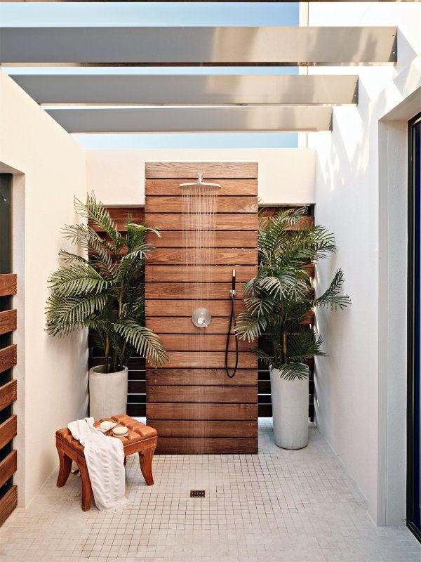 An outdoor shower with a wooden wall and potted plants.