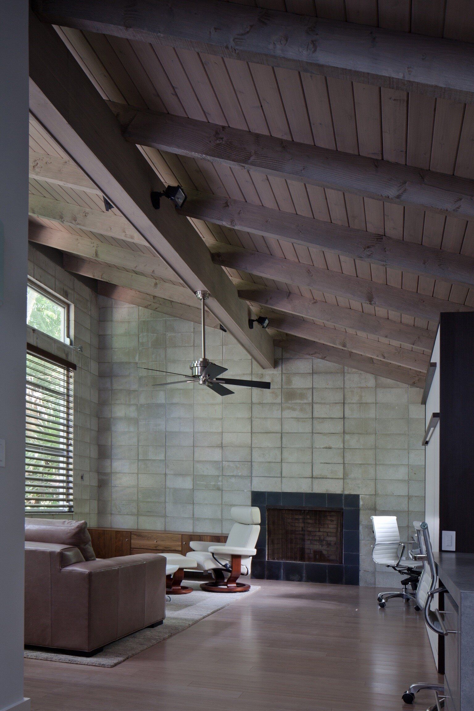 a living room with concrete block walls, a vaulted ceiling, with wooden boards and beams, with a ceiling fan and a fireplace