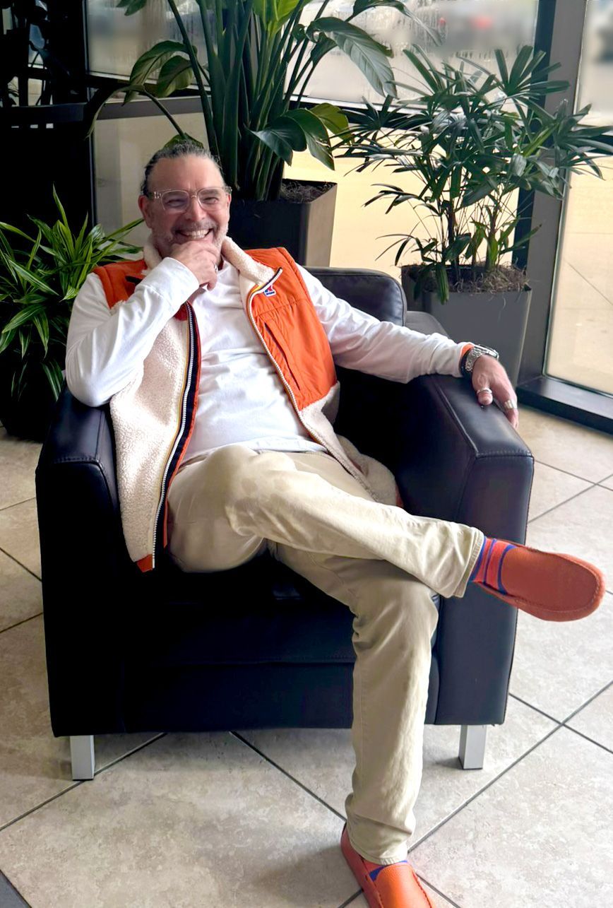 A man is sitting in a chair with his legs crossed and smiling.