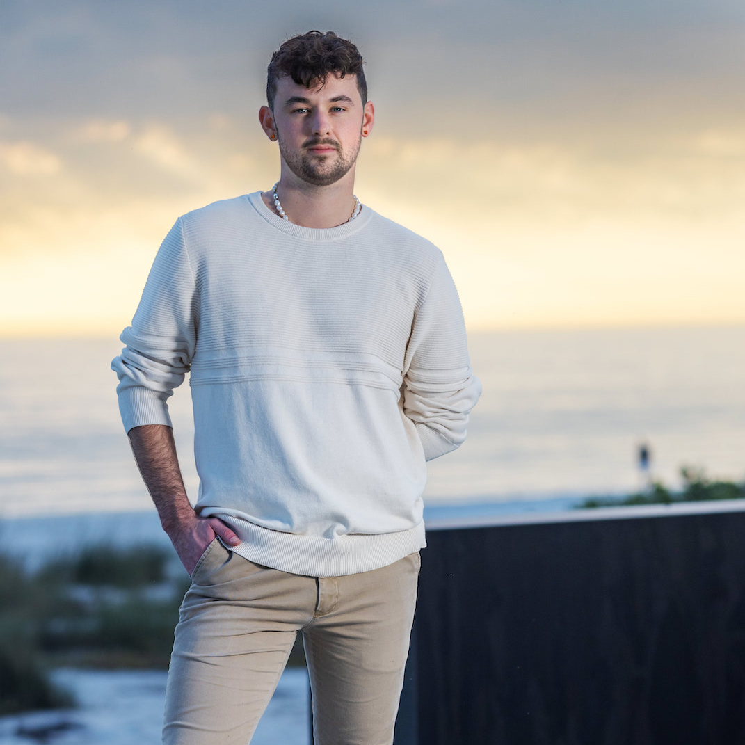 A man in a white sweater is standing with his hands in his pockets