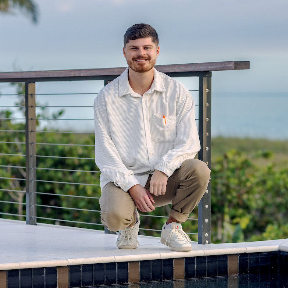 A man is kneeling on a ledge next to a pool.