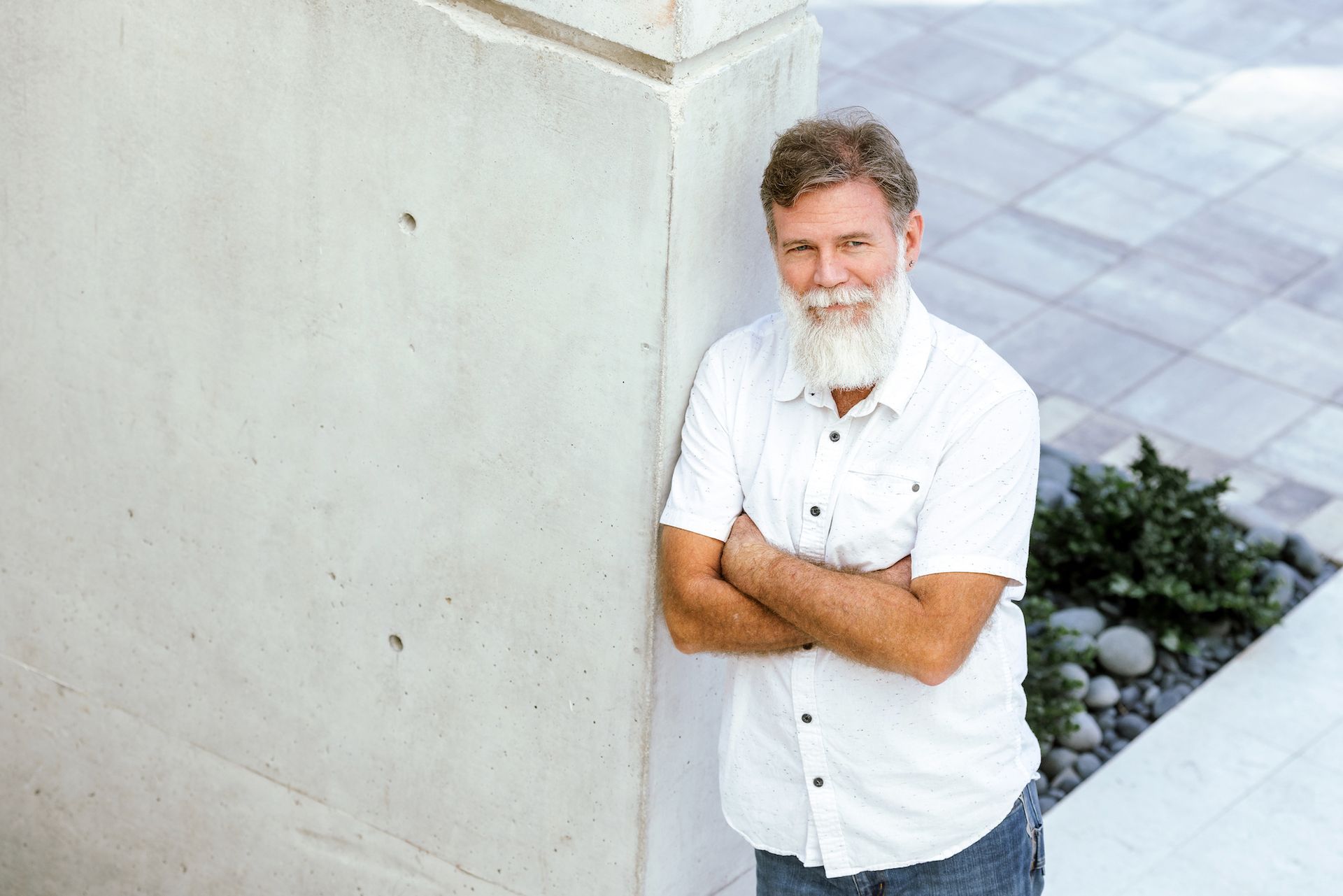 A man with a beard is leaning against a wall with his arms crossed.