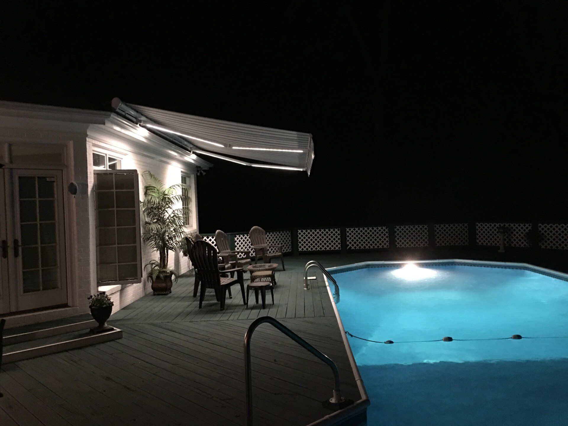 A swimming pool is lit up at night in front of a house.