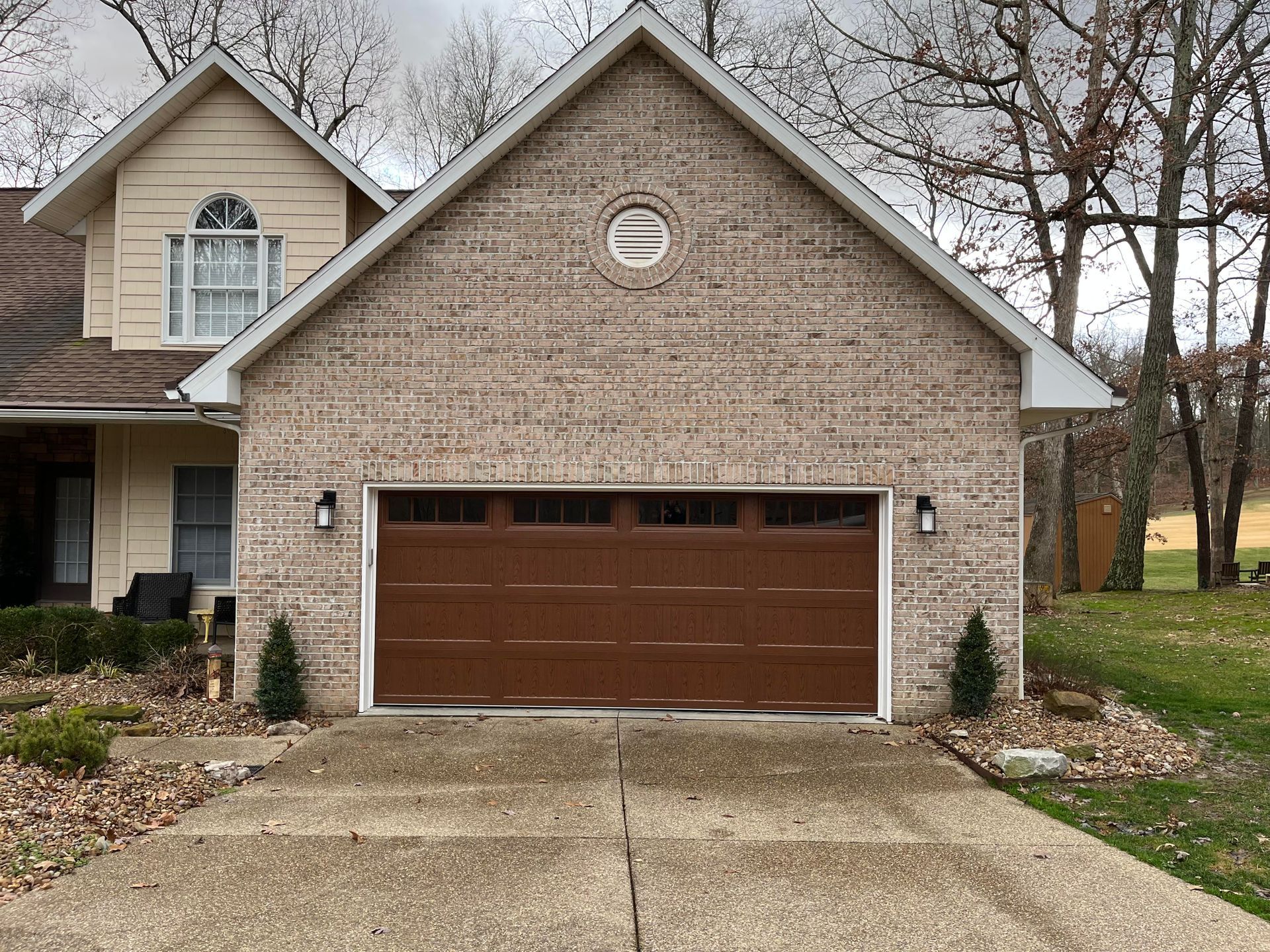 A brown garage door is sitting in front of a brick house.