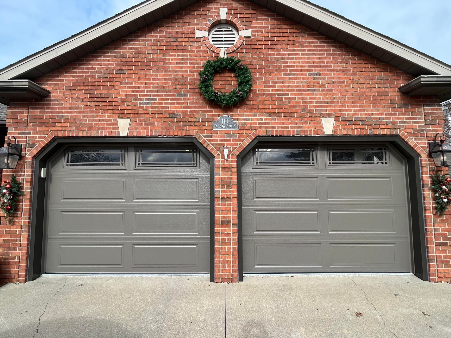A brick house with two garage doors and a wreath on top of them.
