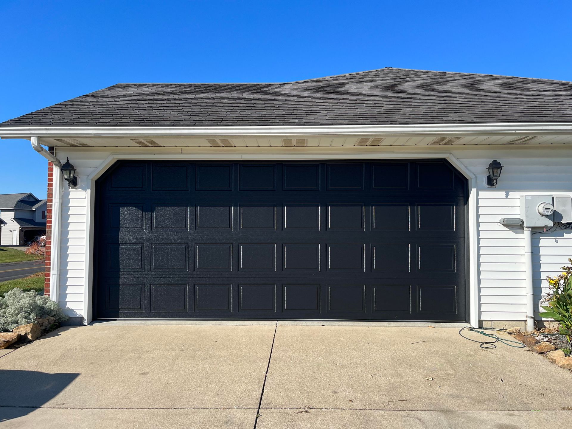 A black garage door is sitting in front of a white house.