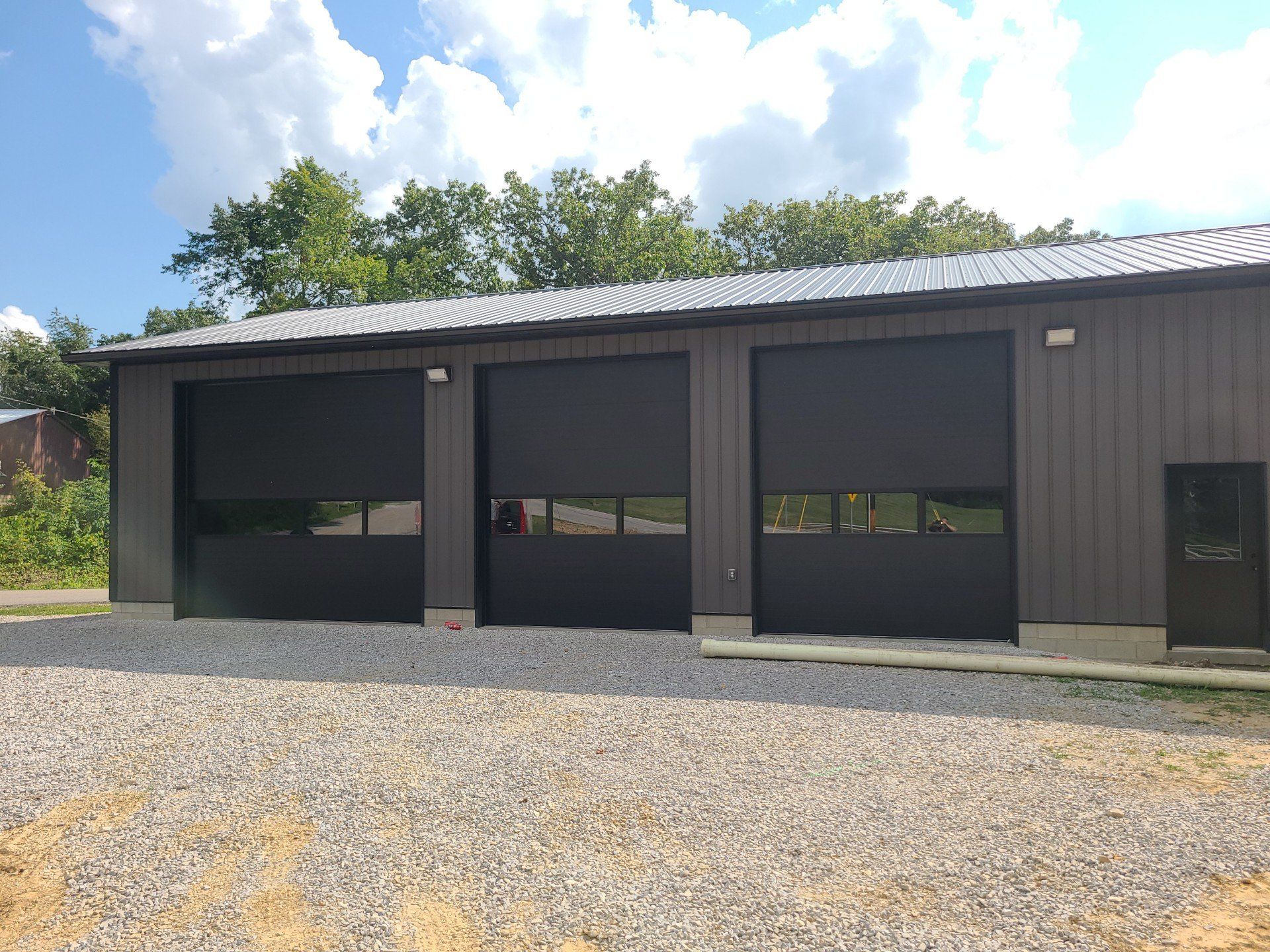 A large garage with three black garage doors is sitting on top of a gravel lot.