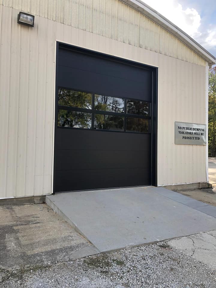 A white building with a black garage door and a ramp.