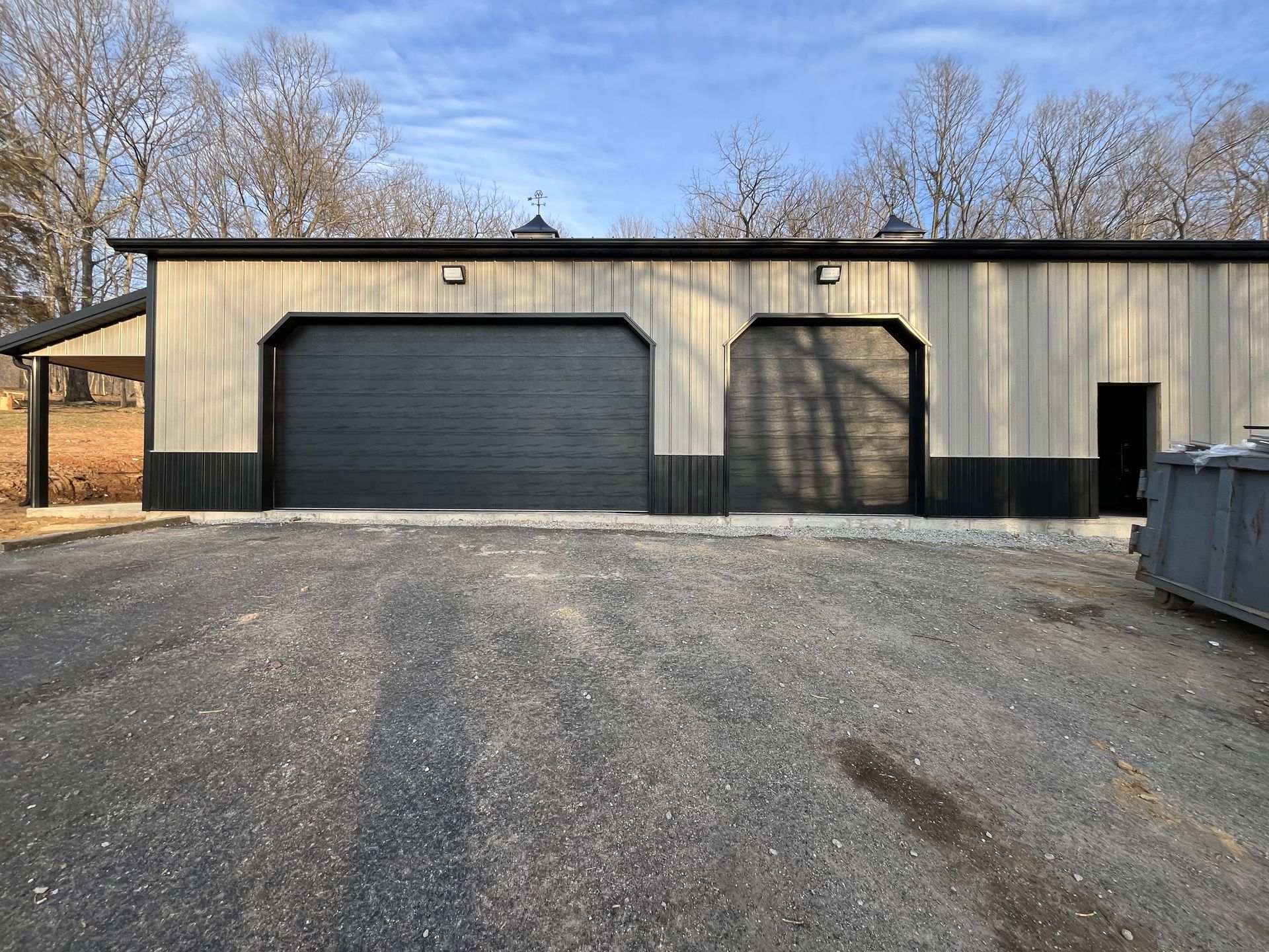 A garage with two garage doors and a dumpster in front of it.
