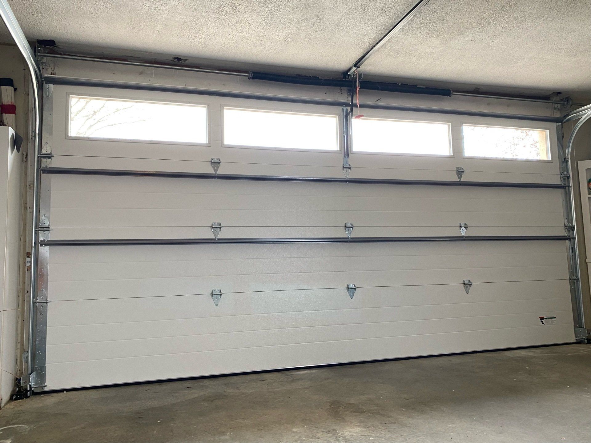 A white garage door with two windows is open in a garage.