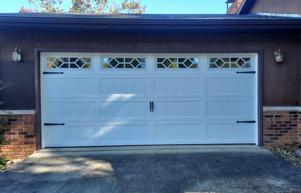 A white garage door is sitting in front of a brown house.