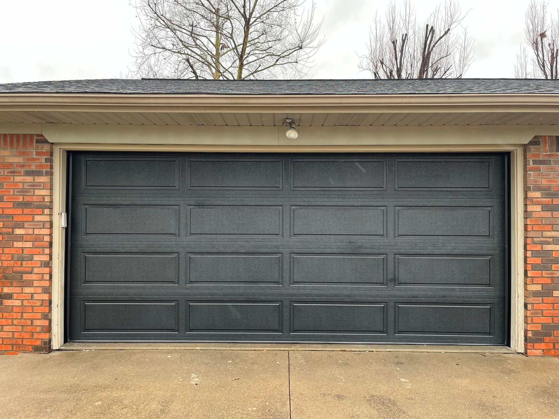 A black garage door is sitting in front of a brick building.