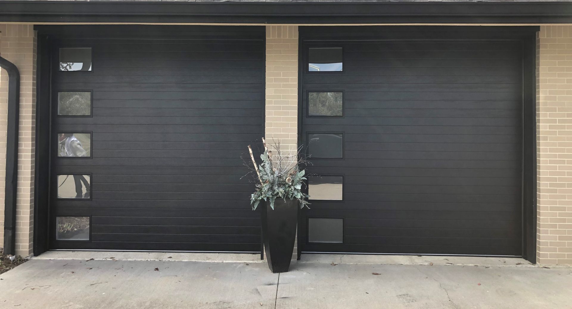 A black garage door with a potted plant in front of it.