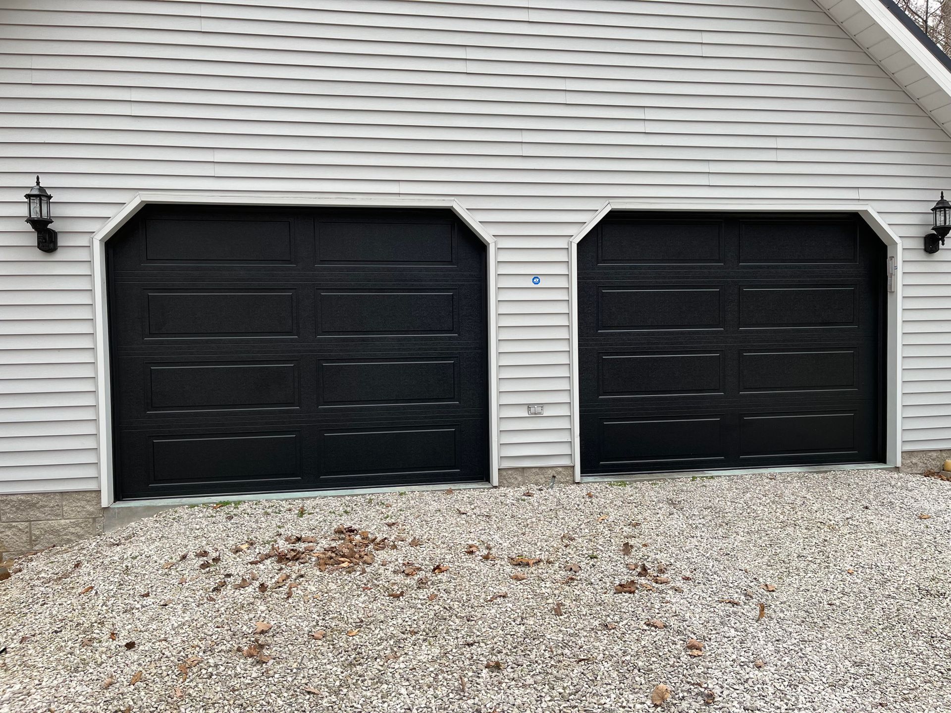There are two black garage doors on a white house.