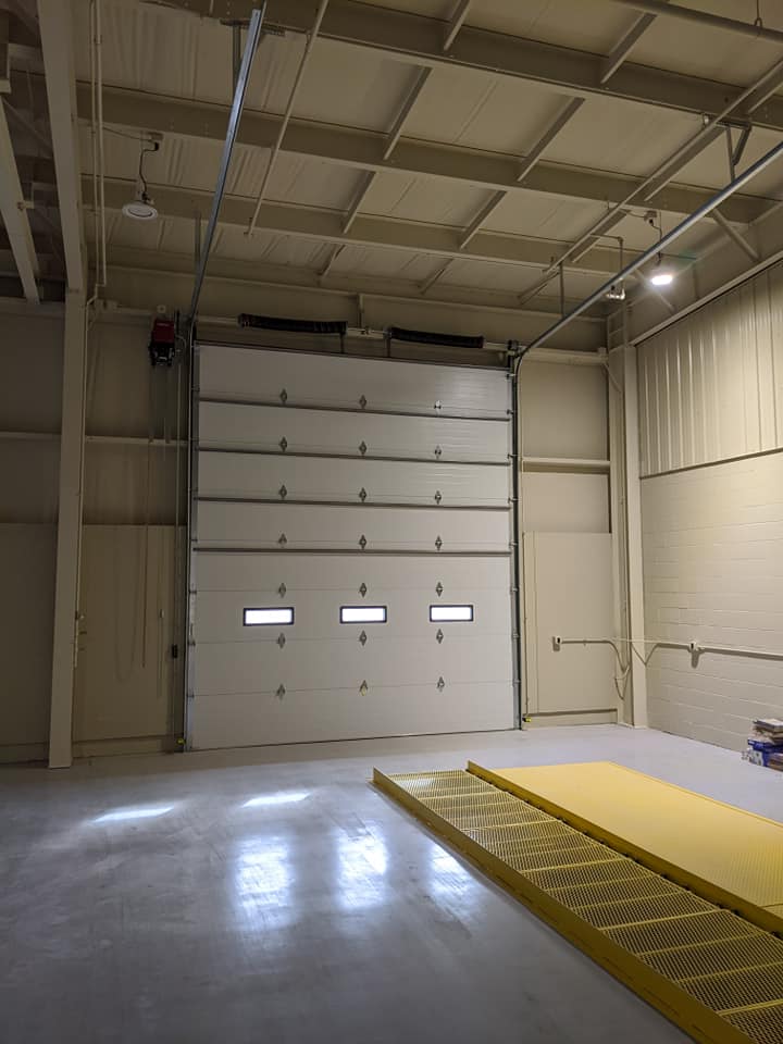 An empty warehouse with a large garage door and a yellow mat on the floor.