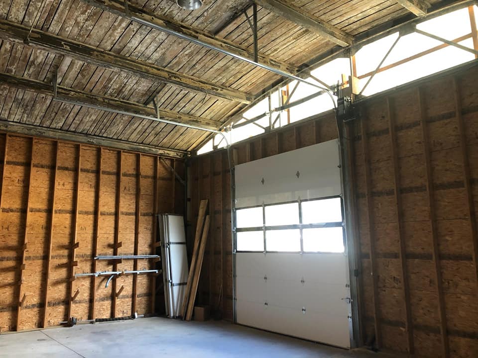 An empty garage with a white garage door and wooden walls.
