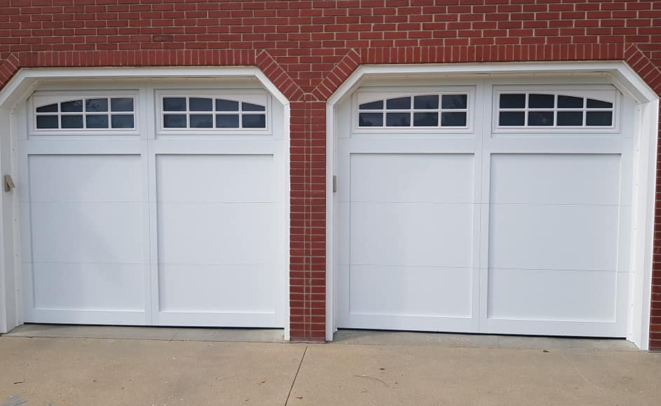 A pair of white garage doors on a red brick building.