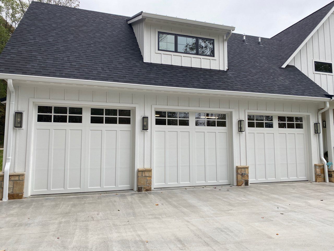 A white house with three garage doors and a black roof.