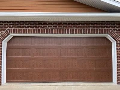 A brown garage door is sitting in front of a brick building.