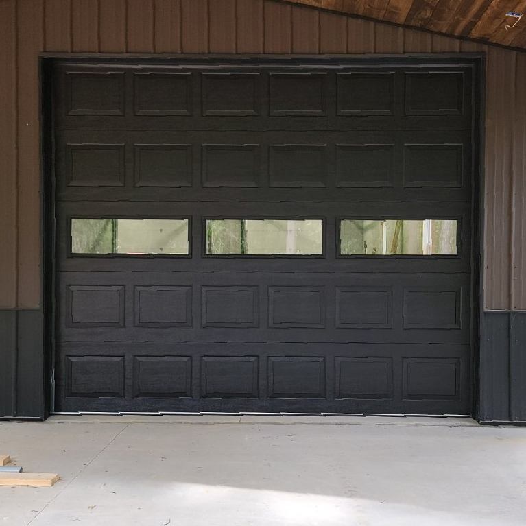 A black garage door with two windows is sitting in a garage.