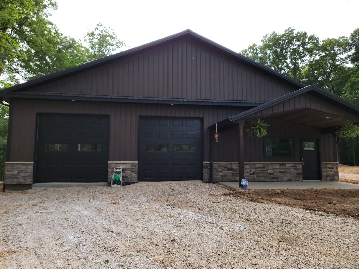 A large brown garage with black garage doors and a porch.