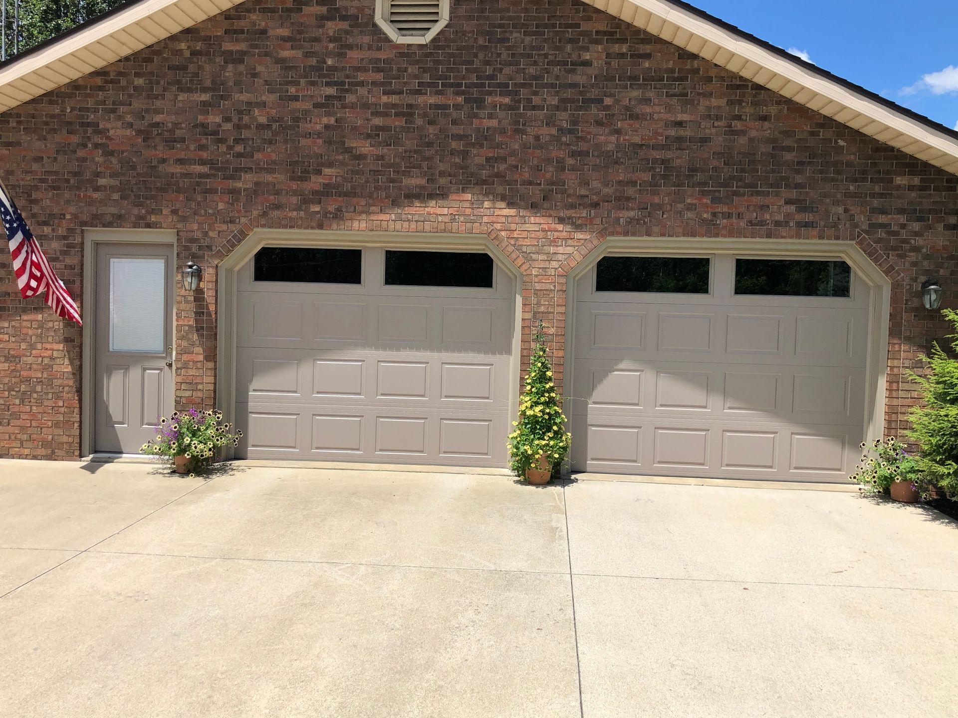 A brick house with two garage doors and an american flag in front of it.
