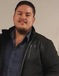 A man with a beard is wearing a black jacket and a blue shirt.