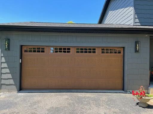 A wooden garage door is sitting in front of a gray house.