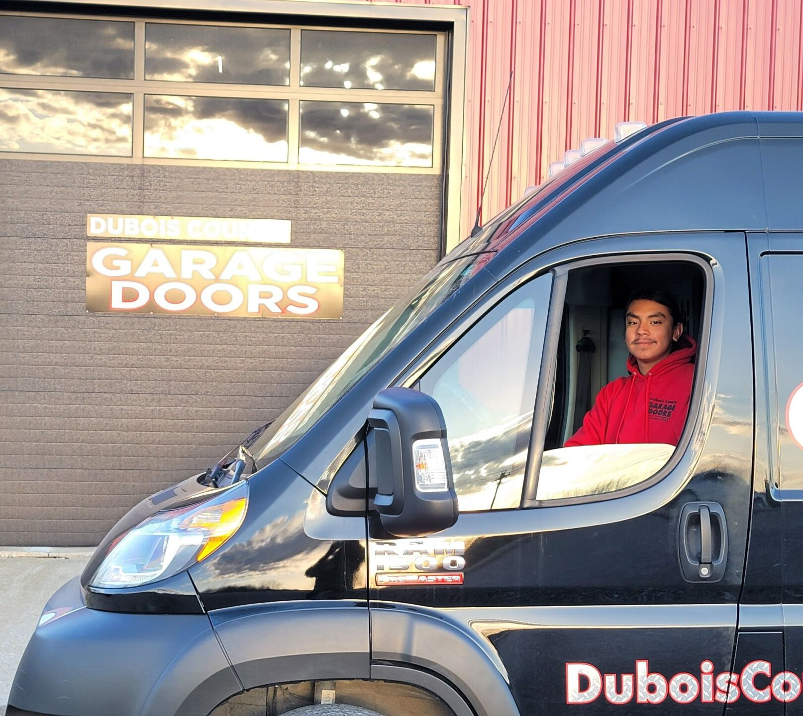 A man is sitting in a black van in front of a garage doors sign