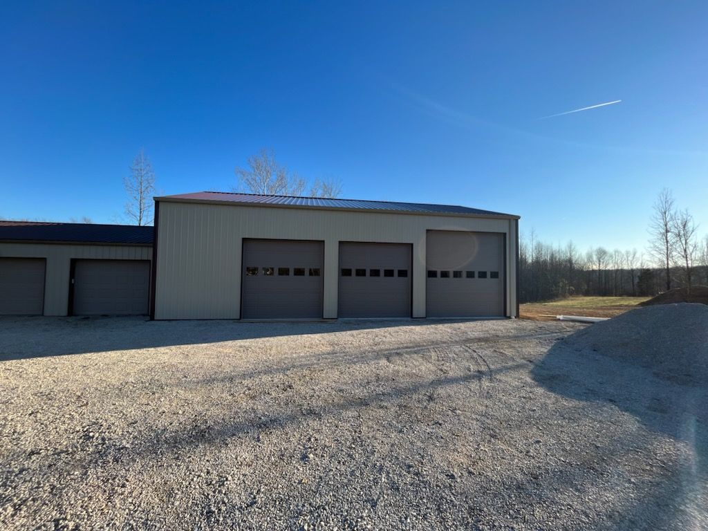 A garage with three garage doors is sitting on top of a gravel lot.