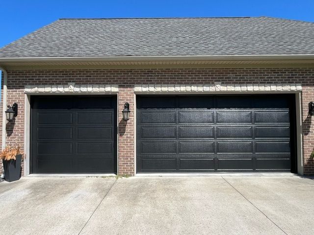 Two black garage doors are on a brick house.