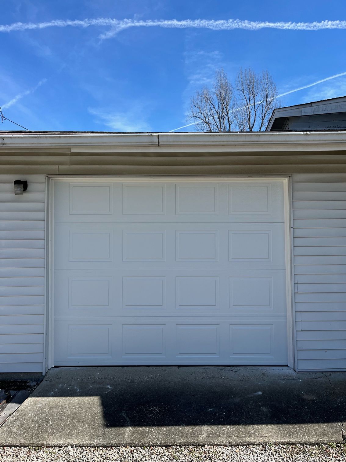 A white garage door on a house with a blue sky in the background.