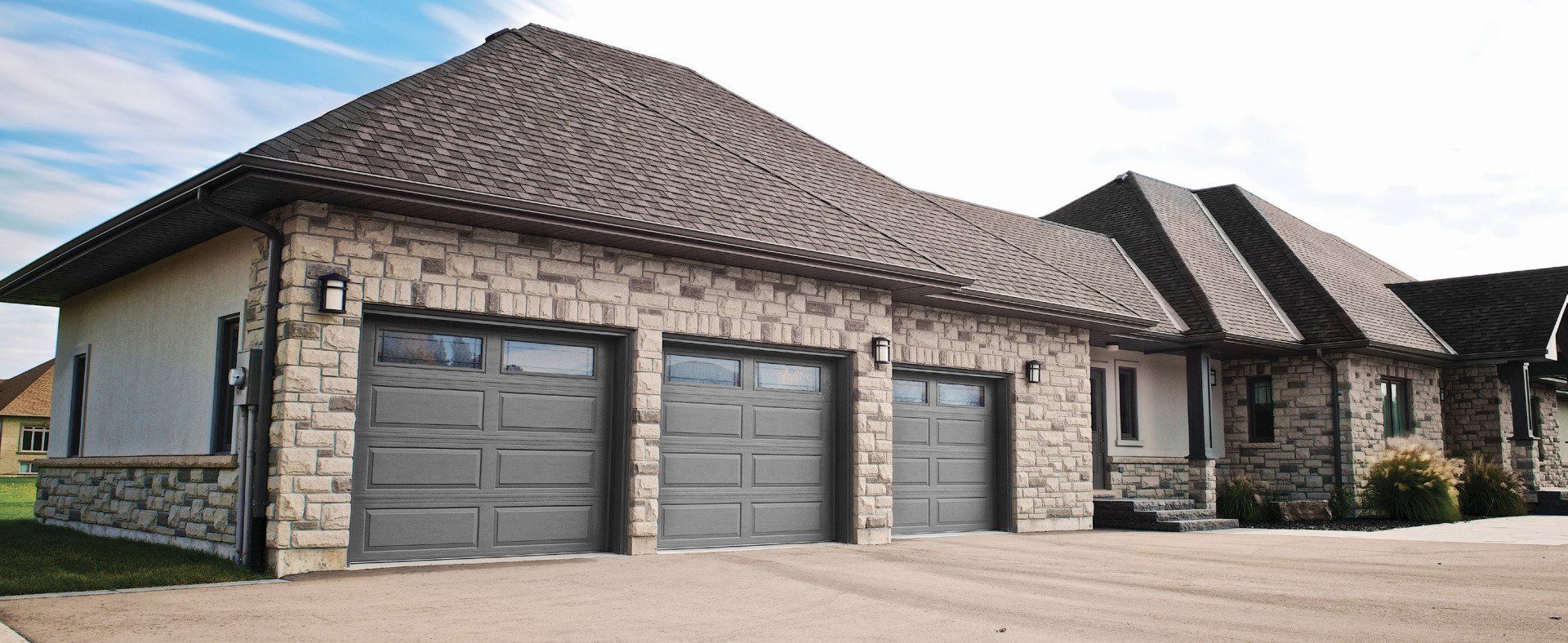 A large house with three garage doors and a stone wall.