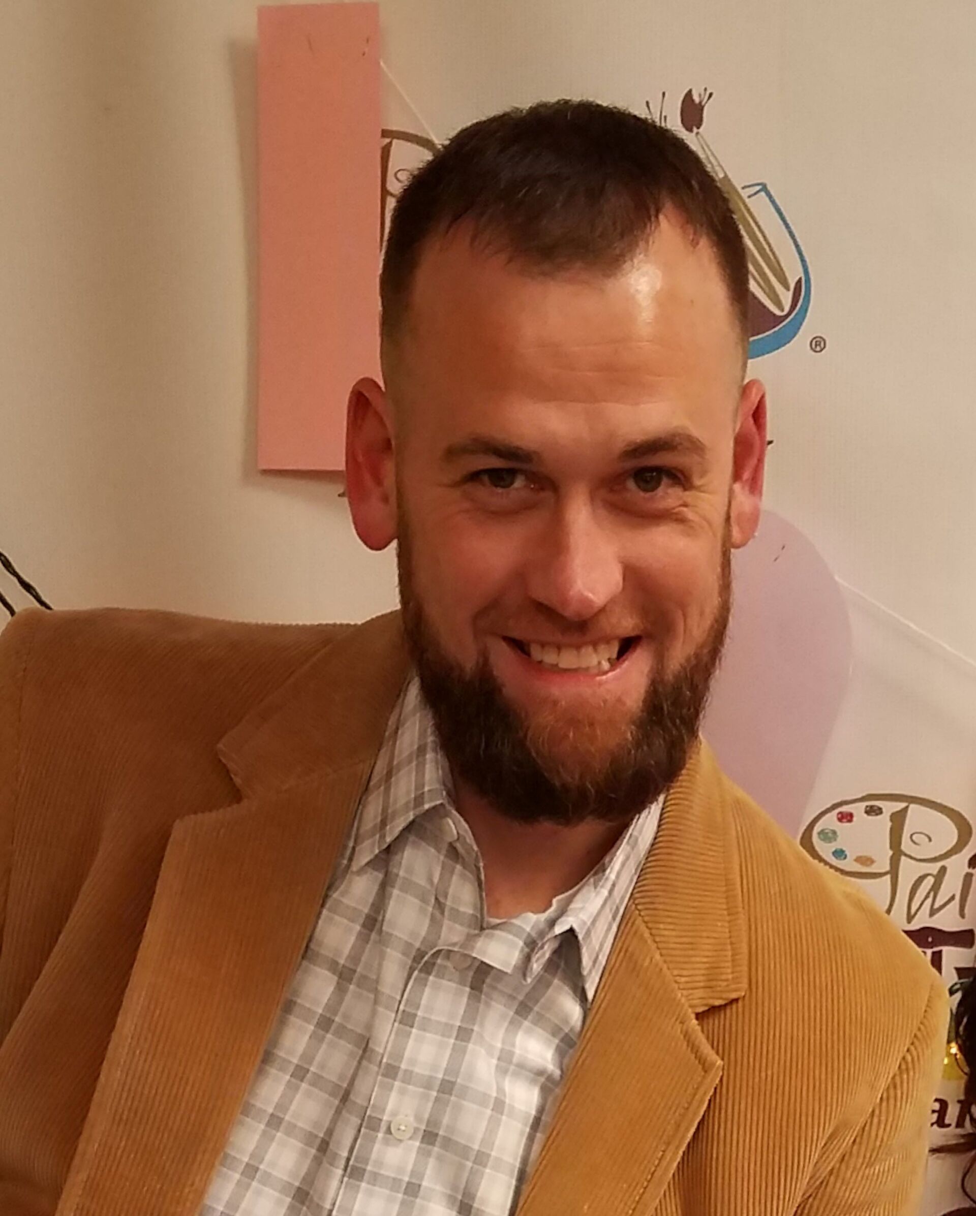 A man with a beard wearing a tan jacket and plaid shirt