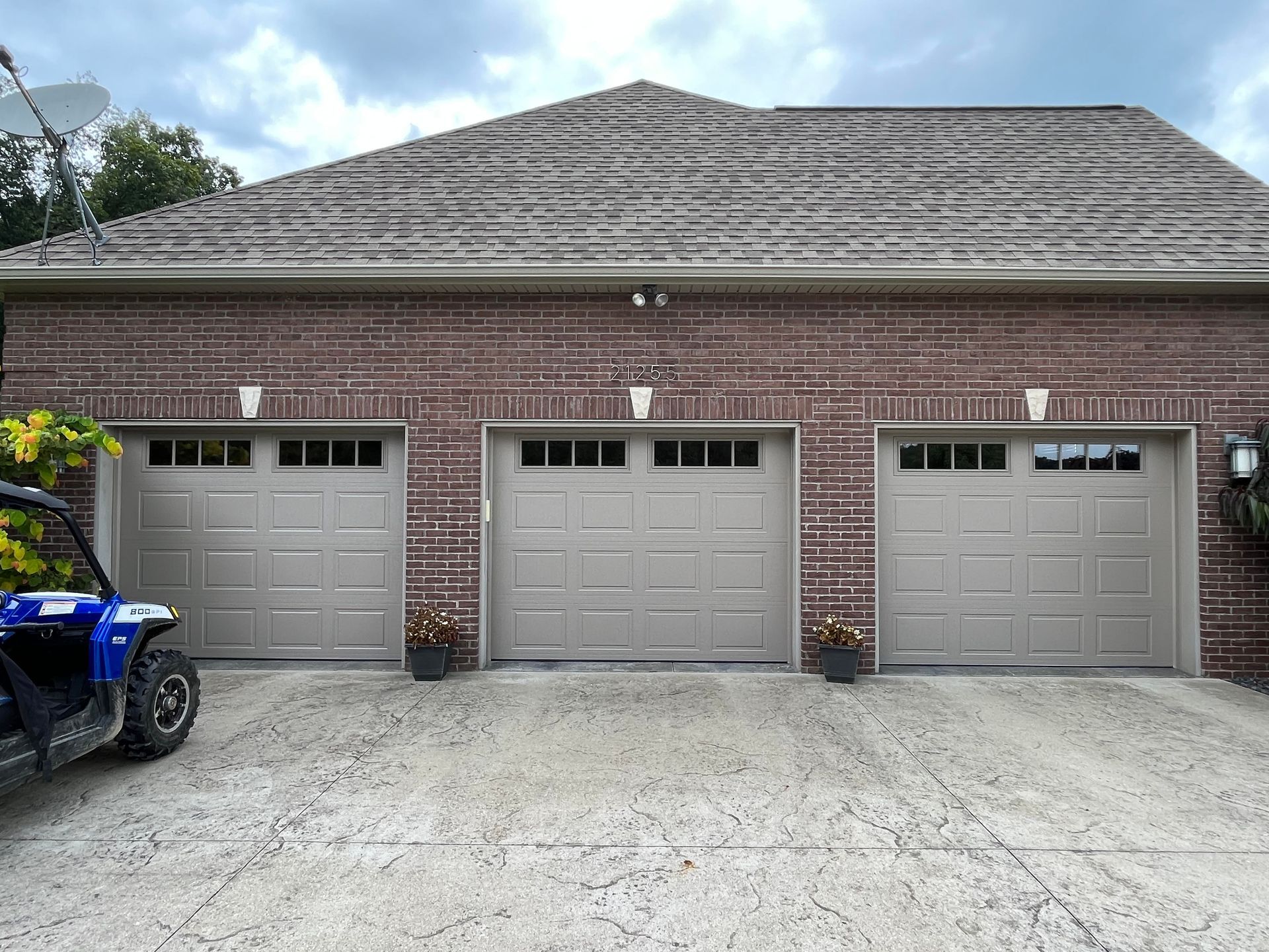 A blue atv is parked in front of a garage with three garage doors.