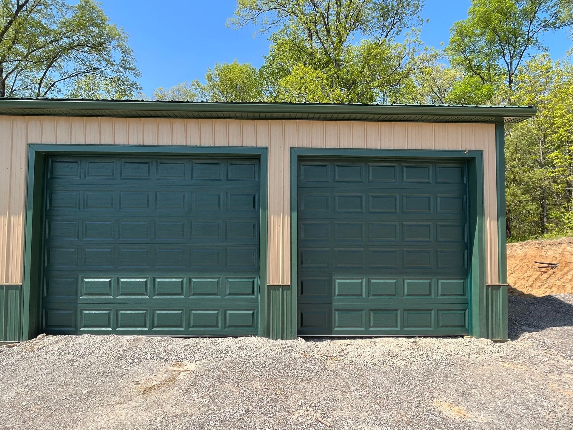 A garage with two green garage doors and trees in the background.