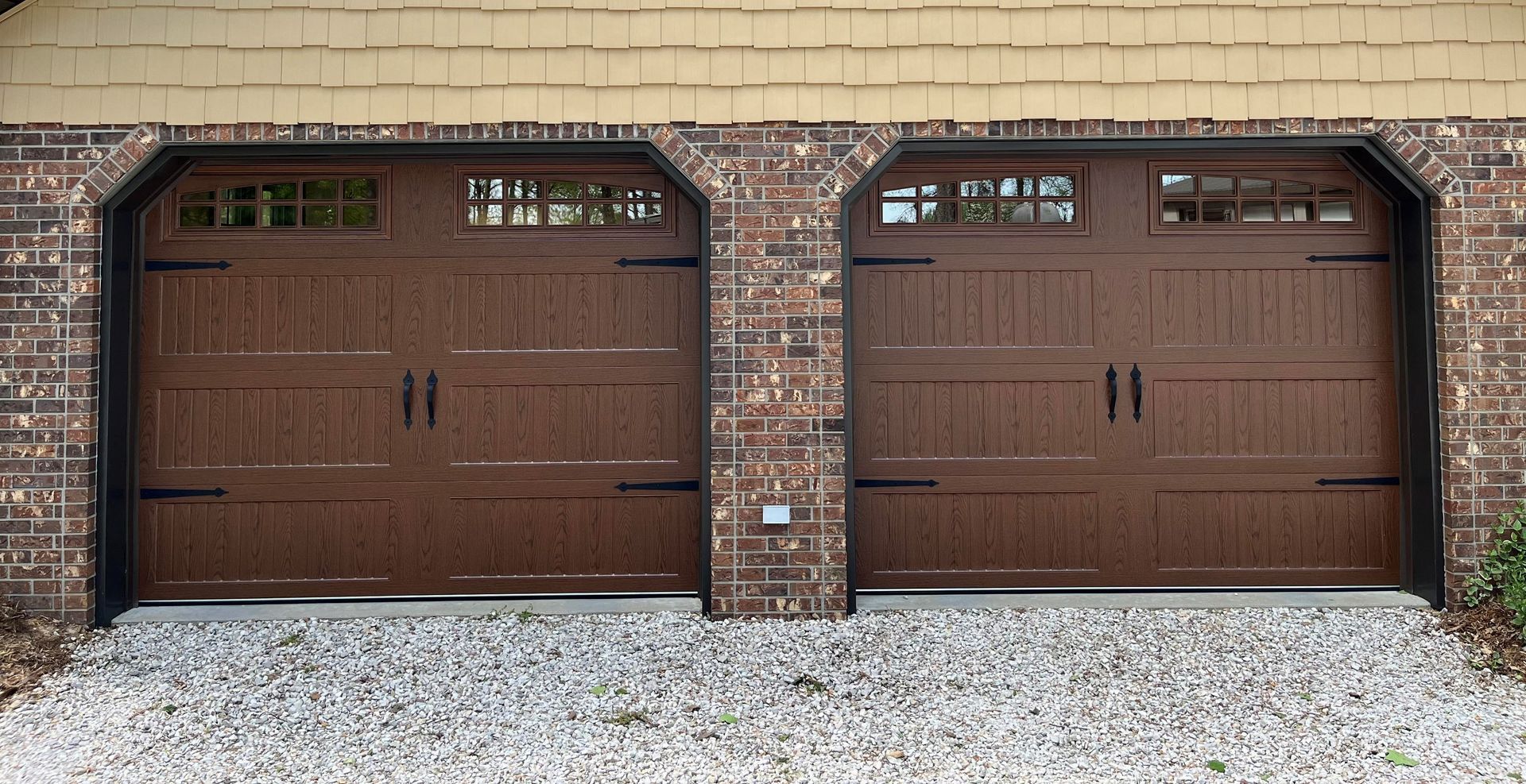 Two brown garage doors are in front of a brick building